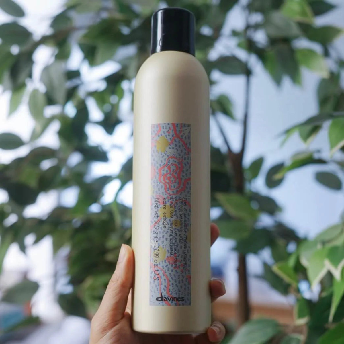 Hand holding a bottle of Davines hair product with a blurred green leafy background