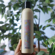 Hand holding a bottle of Davines hair product with a blurred green leafy background