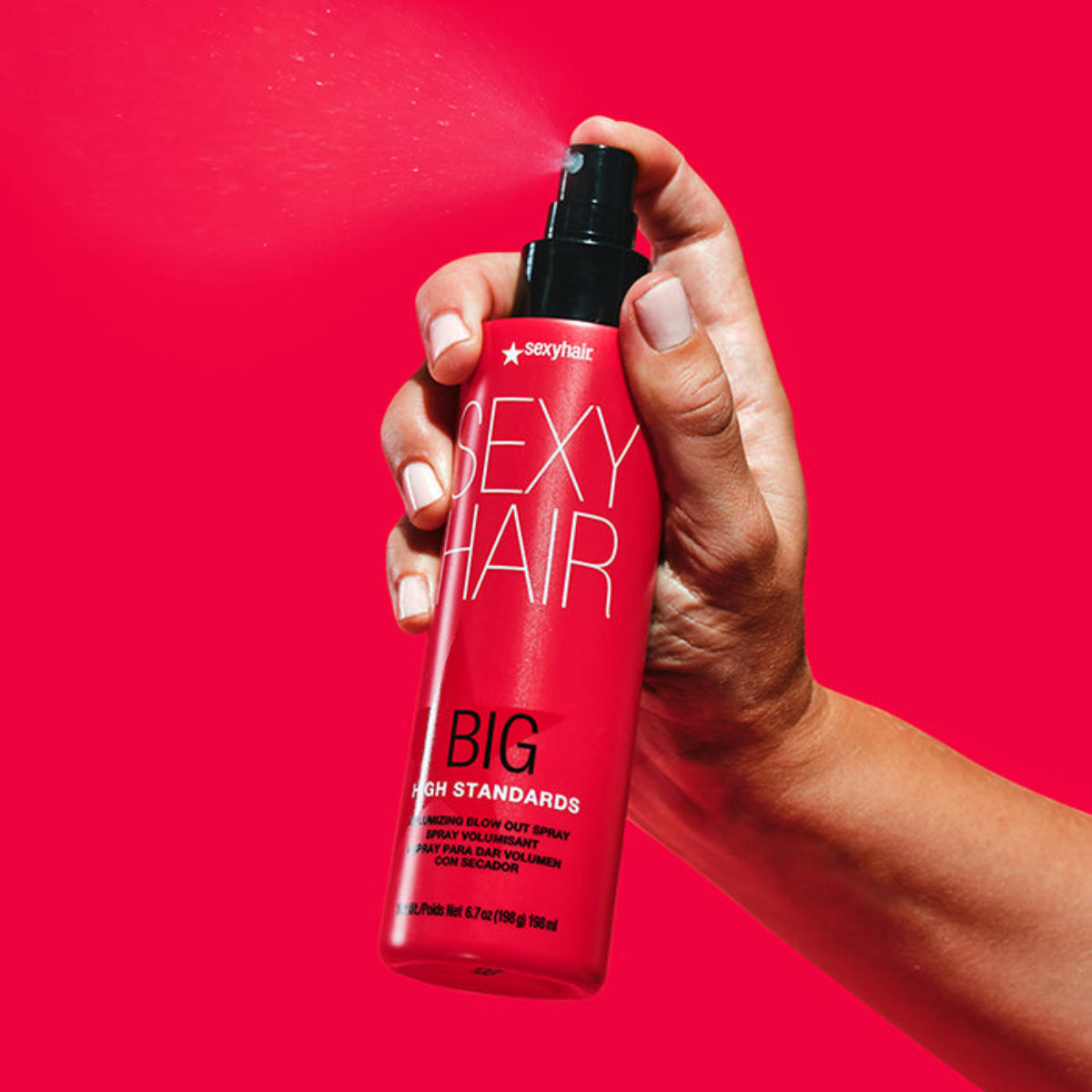 Hand holding a bottle of sexy hair product against a red background