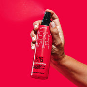 Hand holding a bottle of sexy hair product against a red background